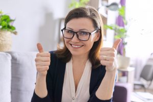 business woman looking at webcam, engaging with client colleagues, shows thumbs up hand sign